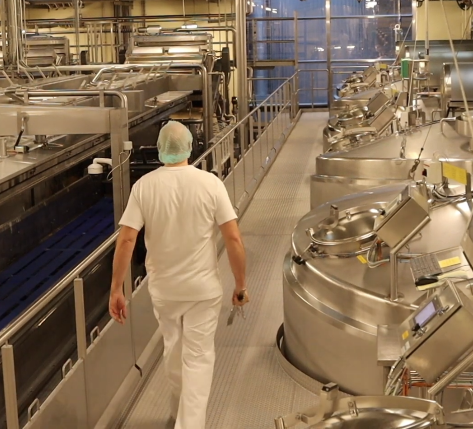 Mejerimedarbejder går igennem mejeriet blandt store kedler 